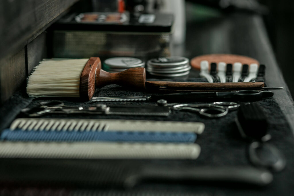 Barber's combs, scissors, a wooden neck brush and grooming tins laid out on a dark bench