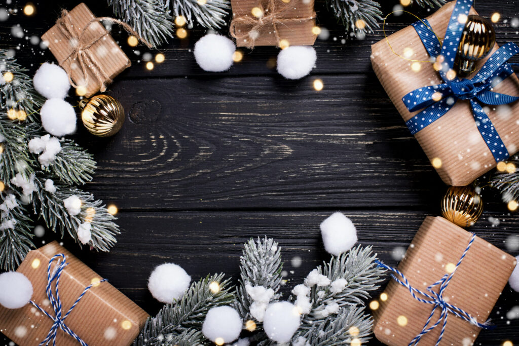 Christmas presents wrapped in kraft paper with blue ribbon, fir branches and gold baubles on a dark wooden table