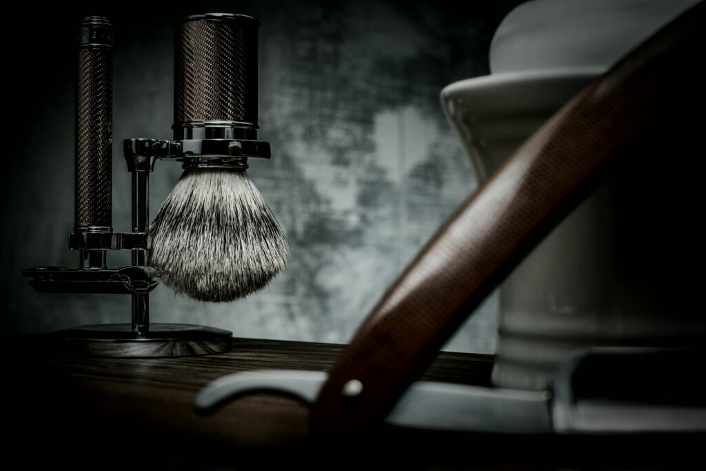 Straight razor and shaving brush on a dark wooden shelf