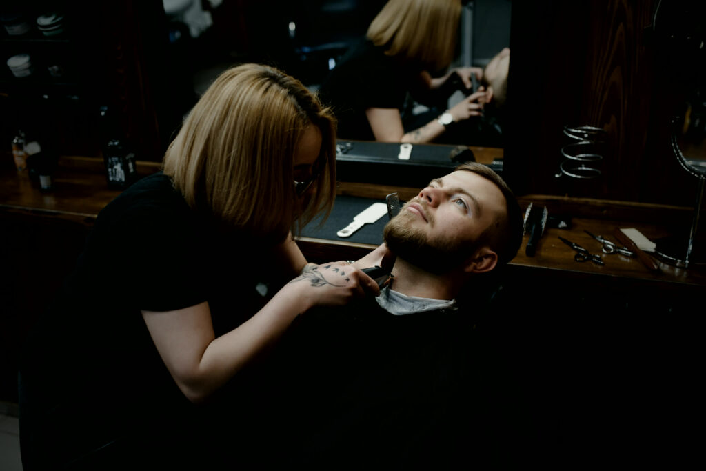 Barber trimming a client's beard in a dark barbershop