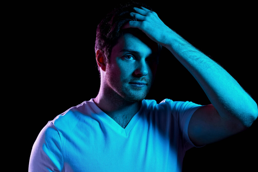 Man running his fingers through short textured hair against a dark background in low cool light